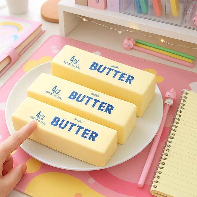 Three bars of butter on a plate with a hand pointing to one of them, set against a colorful background.