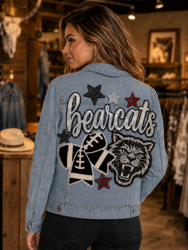 A woman wearing a light blue denim jacket with a custom 'bearcats' football theme patch design on the back, standing inside a rustic retail store.