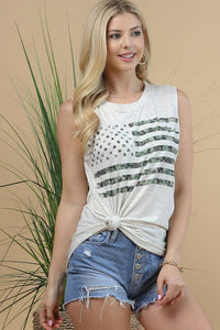 Woman wearing a white sleeveless top with black patterns and denim shorts against a beige background.